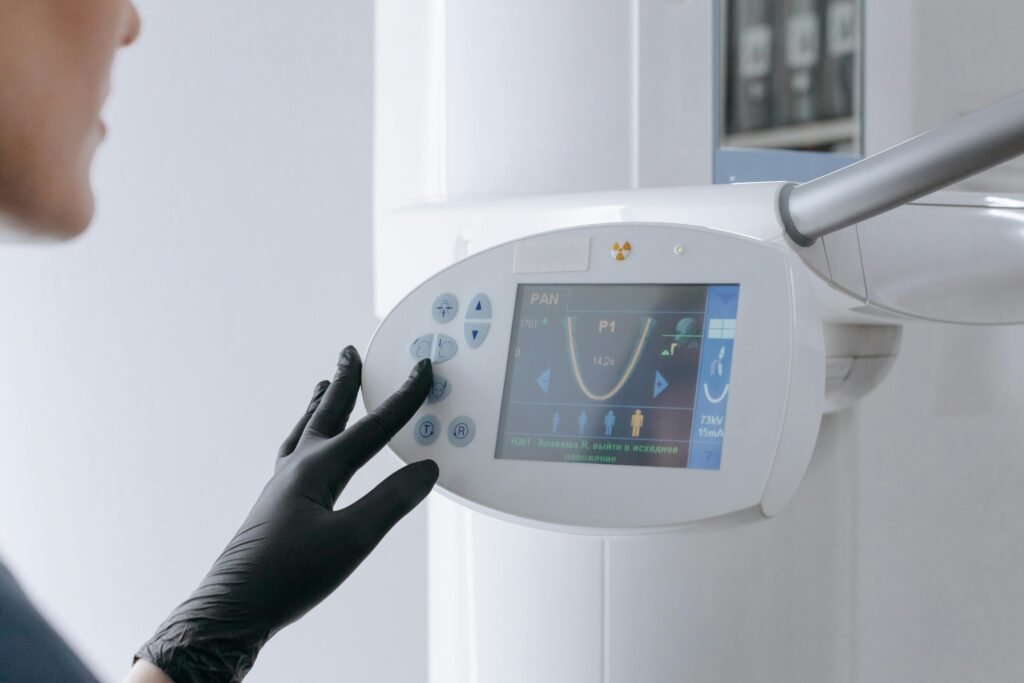Close-up of a dental equipment screen being operated by a gloved hand in a clinic setting.